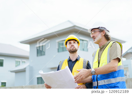 Engineers or construction contractors discussing together at the empty land about construction plan. Man talking to real estate contractor on building blueprint. 120912189
