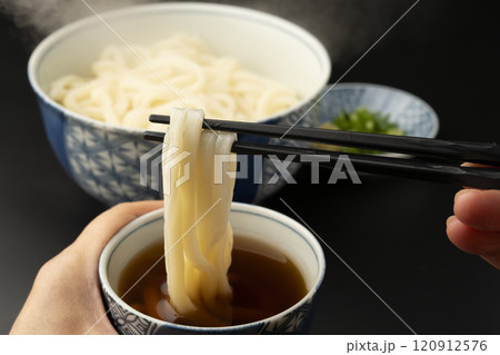うどん　熱々のあつもりうどん　釜揚げうどんをつゆにつけて箸で持ち上げる 120912576