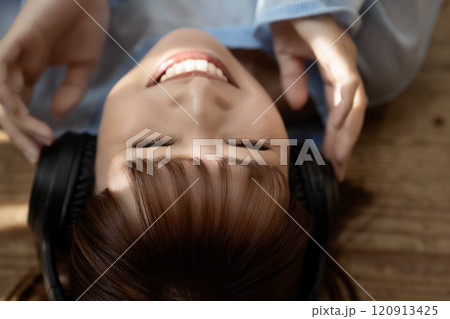 フローリングに寝転んでヘッドホンで音楽を聴く若い女性 120913425