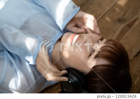 フローリングに寝転んでヘッドホンで音楽を聴く若い女性 120913426