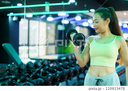 Active Asian sportswoman doing a weight training workout in indoor gym, Asian beautiful woman lifting a dumbbell. 120913478