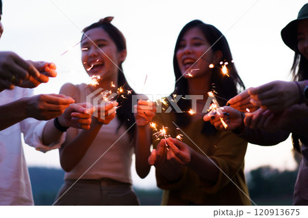 Group of Asian young men and women celebrating together with a sparkling firework in the evening. Happy men and women enjoy playing a sparklers firework in a party. 120913675