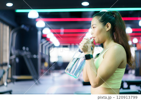 Good looking - beautiful Asian woman relaxing in the gym after made weight training and cardio workout, woman sitting or resting on the bench while drinking water after exercise. 120913799