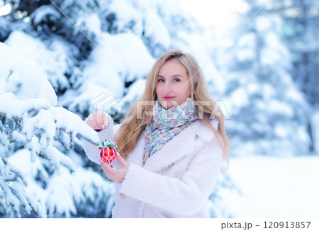 Woman in white coat with a Christmas decoration in winter forest. 120913857