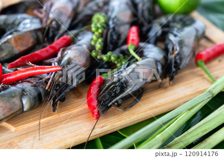 Prawns are artfully arranged on banana leaves, accompanied by fresh green peppercorns, red chilies, and lime. This colorful presentation highlights Asian culinary traditions and flavors. 120914176