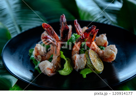 Grilled tiger shrimp are elegantly arranged on banana leaves, surrounded by fresh greens and garnished with lime. This dish evokes a vibrant Asian culinary experience. 120914177