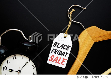 Black Friday Sale on price tag with wooden clothes hanger and alarm clock top view on black background 120914229
