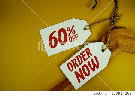 Order Now and Sale 60% on price tag with wooden clothes hanger top view on yellow background Order Now and Sale 60% on price tag with wooden clothes hanger top view on yellow background 120914268