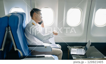 Asian Confident male pilot in uniform leaning at the passenger seat while standing inside of the airplane flight cockpit during takeoff 120921405
