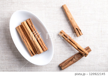 Ceylon cinnamon sticks, cinnamon quills in an oval white bowl on linen. Group of whole dried bark strips of Cinnamomum verum used mainly as warm and earthy aromatic condiment and flavoring additive. 120922145