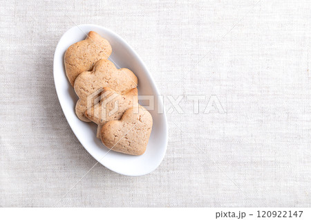 Homemade gingerbread cookies in an oval white bowl on linen with empty space for text. Sweet, light brown and flat baked goods for Christmas season, flavored with ginger, cloves, nutmeg, and cinnamon. 120922147