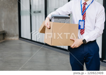 Businessman sitting outside the office with a box of belongings, reflecting on job loss. Capturing the emotional impact and reality 120922409