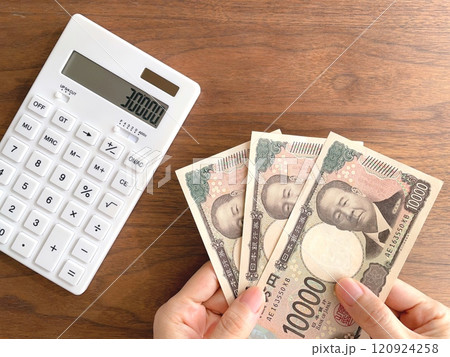 3万円を持つ女性の手と机上の電卓 120924258