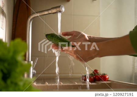 Washing a fresh cucumber under running water for a healthy salad preparation 120927191