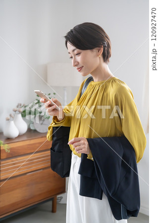 屋内で鞄とジャケットを持ってスマホを手にする女性 屋内で鞄とジャケットを持ってスマホを手にする女性 120927470