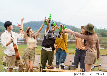 Group of Asian young adult people enjoy drinking a beer together during camping at the park. Asian young women and men celebrating with a bottle of a beer together. 120929371