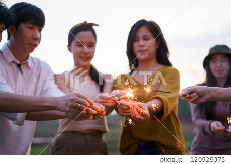 Group of Asian young men and women celebrating together with a sparkling firework in the evening. Happy men and women enjoy playing a sparklers firework in a party. Group of Asian young men and women celebrating together with a sparkling firework in the evening. Happy men and women enjoy playing a sparklers firework in a party. 120929373