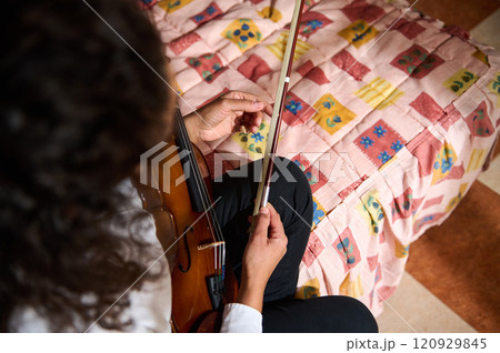 Close-up of a person tuning a violin on a colorful bedspread Close-up of a person tuning a violin on a colorful bedspread 120929845