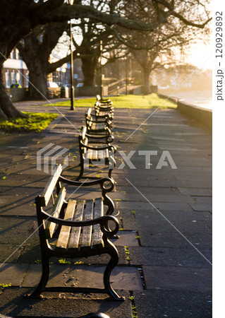 明るい夜明けの朝日を浴びるテームズ川沿いの公園に置かれた歴史的なベンチ ロンドン郊外のキューにて 明るい夜明けの朝日を浴びるテームズ川沿いの公園に置かれた歴史的なベンチ ロンドン郊外のキューにて 120929892
