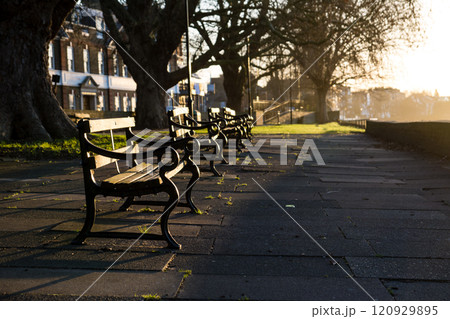 明るい夜明けの朝日を浴びるテームズ川沿いの公園に置かれた歴史的なベンチ ロンドン郊外のキューにて 明るい夜明けの朝日を浴びるテームズ川沿いの公園に置かれた歴史的なベンチ ロンドン郊外のキューにて 120929895