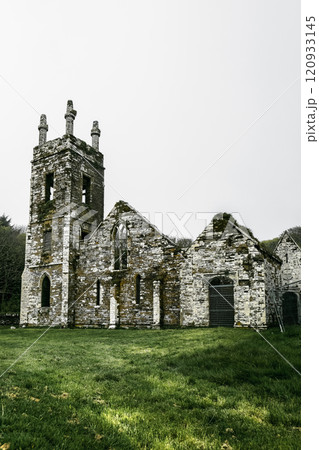 In a peaceful rural setting, historic stone church ruins with moss-covered walls under a cloudy sky. 120933145