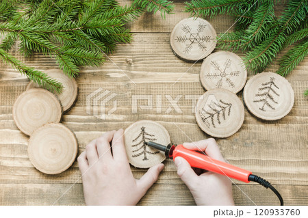 Christmas or New Year homemade pyrography toys. Wooden slice. Xmas decorations. Child makes gifts for relatives. View from above. 120933760