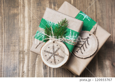 Christmas gift box in rustic style wrapped in craft paper with decor of wooden sliced with woodburning symbol. 120933767