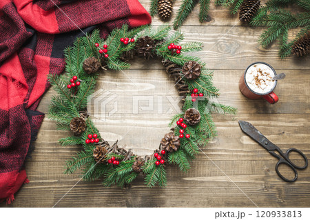 Christmas composition of wreath, checkered pleid, cup of coffee on wooden board. Flat lay. Top view. Copy space. Xmas card 120933813