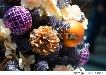 Design Christmas tree with holiday golden cones and purple balls on blurred bokeh background in mall. Xmas card. Close up. 120933844