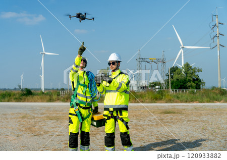 Wind turbine or windmill workers use drone to work in workplace field during day time with one point to the drone and wind turbine are in the background. Wind turbine or windmill workers use drone to work in workplace field during day time with one point to the drone and wind turbine are in the background. 120933882