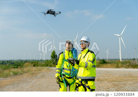 Two wind turbine or windmill workers use drone to work in workplace field during day time and wind turbine are in the background. 120933884