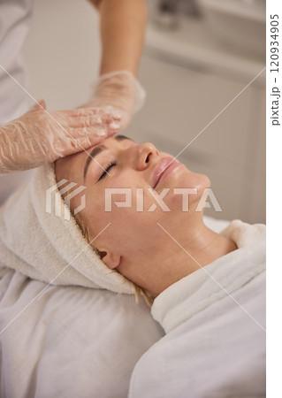 Skin care, Skin analysis, Facial steam. Proficient esthetician softly massages female client's face, providing calming facial in hygienic and well-lit clinical environment. Skin care, Skin analysis, Facial steam. Proficient esthetician softly massages female client's face, providing calming facial in hygienic and well-lit clinical environment. 120934905