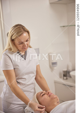 lifting massage, aesthetic salon, beauty spa. Beautiful female has facial massage in beauty clinic, young woman's face lying on back, getting face lifting massage in beauty spa concept, towel on head lifting massage, aesthetic salon, beauty spa. Beautiful female has facial massage in beauty clinic, young woman's face lying on back, getting face lifting massage in beauty spa concept, towel on head 120934906
