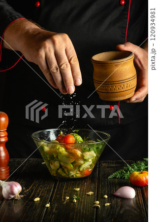 In a cozy kitchen with wooden accents, a chef artfully sprinkles salt over a vibrant salad filled with fresh vegetables. The warm ambiance enhances the culinary artistry taking place In a cozy kitchen with wooden accents, a chef artfully sprinkles salt over a vibrant salad filled with fresh vegetables. The warm ambiance enhances the culinary artistry taking place 120934981