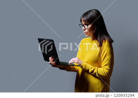 Serious middle aged woman using laptop on grey background 120935294
