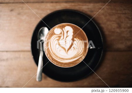 Artistic latte with foam design served in a black cup on table 120935900