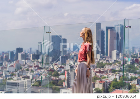 Female tourist or businesswoman standing on a skyscraper rooftop with a panoramic view of Mexico City. Travel or international business in Mexico concept 120936014