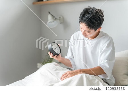 目覚まし時計を見て朝起床する男性(体調不良・疲労・睡眠・覚醒・眠り) 目覚まし時計を見て朝起床する男性(体調不良・疲労・睡眠・覚醒・眠り) 120938388