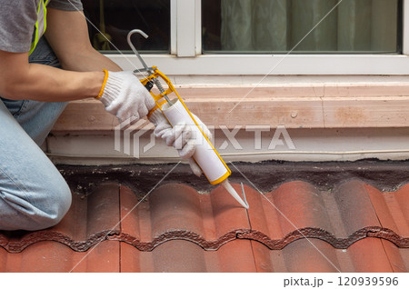 Construction worker using silicone sealant adhesive to fix crack of the old tile roof. 120939596