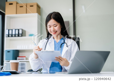 Confident young  female doctor in white medical uniform sit at desk working on computer. Smiling use laptop 120940642