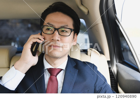後部座席に座りスマホで話すビジネスマン 120940890