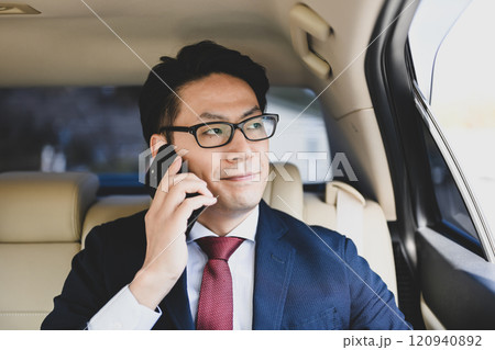 後部座席に座りスマホで話すビジネスマン 120940892