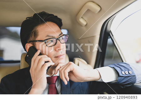 後部座席に座りスマホで話すビジネスマン 120940893