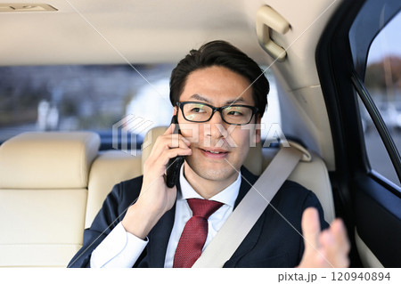 後部座席に座りスマホで話すビジネスマン 120940894