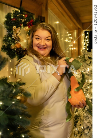 Woman Christmas Decorations Holiday Cheer - A woman smiles near Christmas decorations in her home. Woman Christmas Decorations Holiday Cheer - A woman smiles near Christmas decorations in her home. 120941952