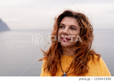 Portrait windswept hair happy woman against a backdrop of mountains and sea. Daylight illuminates the tranquil outdoor setting Portrait windswept hair happy woman against a backdrop of mountains and sea. Daylight illuminates the tranquil outdoor setting 120941990