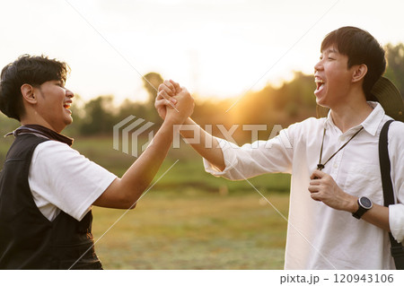 Happy Asian men looking at the beautiful sunlight during the sunset behind mountain together. Friends touch - hold hands together. 120943106