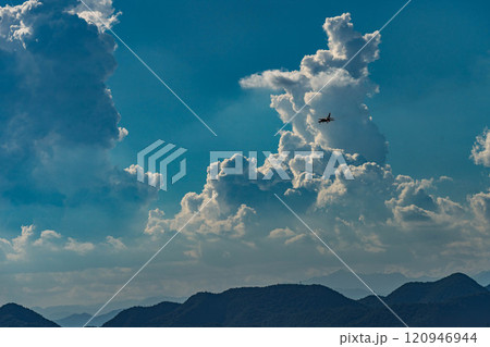 青空に浮かぶ白い雲に飛び去る飛行機 120946944