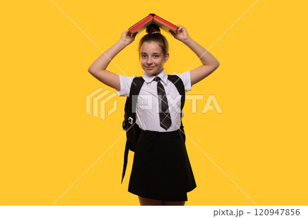 Teen girl holding book over head, wearing school uniform 120947856