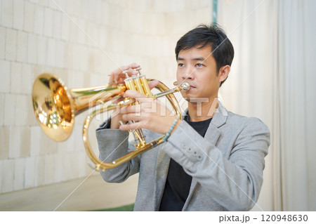 Asian man plays cornet. A solo Asian skillful musician is playing or practicing cornet in the restaurant. A man enjoy playing cornet or trumpet. Asian man plays cornet. A solo Asian skillful musician is playing or practicing cornet in the restaurant. A man enjoy playing cornet or trumpet. 120948630